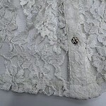 Close-up of a white lace dress with intricate floral patterns and decorative buttons, showcasing fine craftsmanship and delicate fabric.
