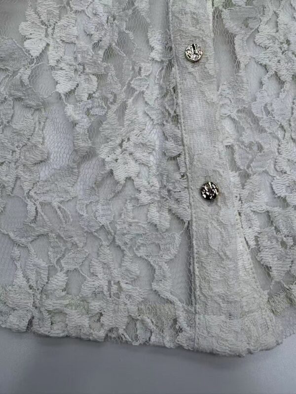 Close-up of a white lace dress with intricate floral patterns and decorative buttons, showcasing fine craftsmanship and delicate fabric.