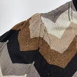 Close-up of a multicolored knit sweater featuring earthy tones like beige, brown, black, and cream, showcasing intricate patterns and textured fabric.