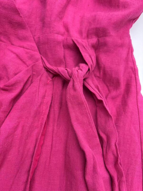 Close-up of a vibrant pink linen dress featuring a tied waist detail, showcasing soft fabric texture and elegant design for stylish summer wear.
