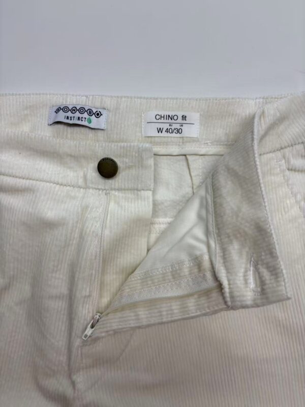 Close-up of cream-colored men's chino pants with zipper and button closure, showing fabric texture and fit details.