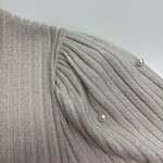 Close-up of a beige ribbed knit sweater featuring pearl embellishments on the shoulder for a stylish look.