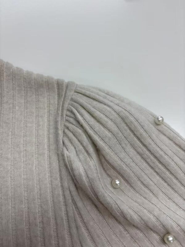 Close-up of a beige ribbed knit sweater featuring pearl embellishments on the shoulder for a stylish look.
