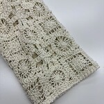 Close-up of intricate handmade crochet lace fabric in cream color, showcasing detailed floral and geometric patterns, ideal for fashion and home decor.