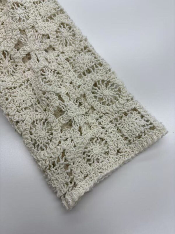 Close-up of intricate handmade crochet lace fabric in cream color, showcasing detailed floral and geometric patterns, ideal for fashion and home decor.