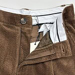 Close-up of brown corduroy men's pants with zipper and button closure, showcasing textured fabric and detailed stitching.