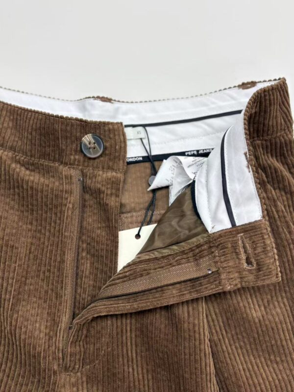 Close-up of brown corduroy men's pants with zipper and button closure, showcasing textured fabric and detailed stitching.