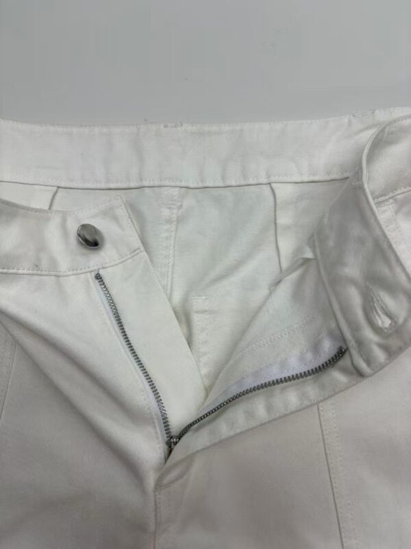 Close-up of stylish white pants with zipper and button details, perfect for modern fashion looks.