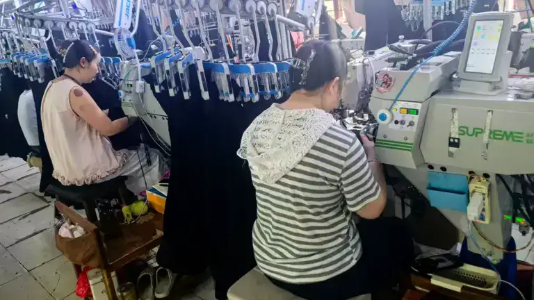 Workers operating industrial sewing machines in a textile manufacturing facility for apparel production.