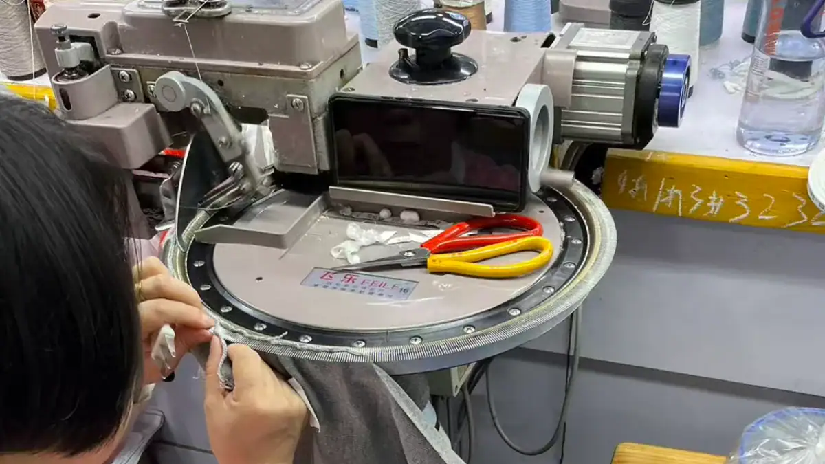 Close-up of a linking machine used for sewing sweater seams, with tools and fabric in a textile manufacturing setting.