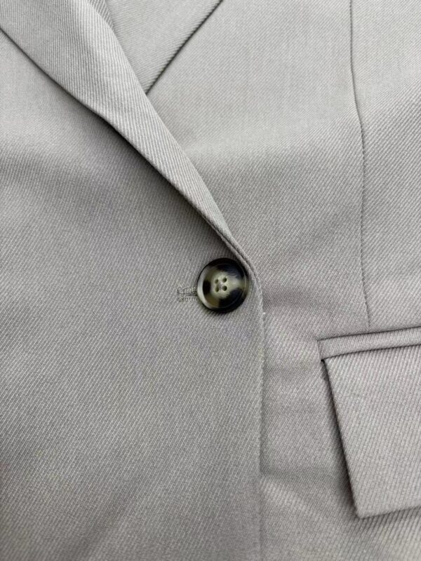 Close-up of a grey suit jacket with a single button and tailored lapel, showcasing professional men's fashion and formal wear.