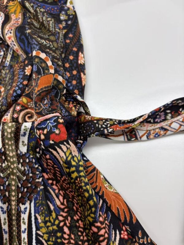 Vibrant bohemian patterned scarf with intricate designs in orange, blue, black, and white, tied in a knot on a white background.