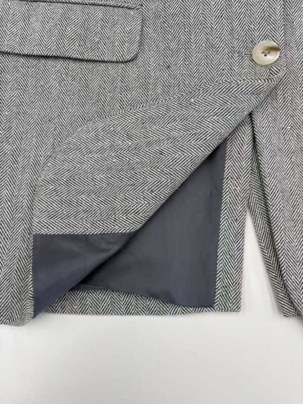 Close-up of men's herringbone wool blazer with a single button and inner lining, showcasing classic tailored design and high-quality fabric.