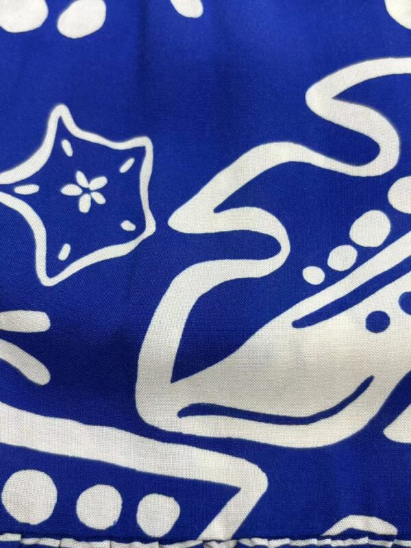 Close-up of blue fabric with white holiday-themed patterns including stars, swirls, and dots, suitable for Christmas or winter decorations.