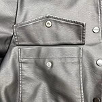 Close-up of a silver leather jacket featuring two front pockets with snap buttons, showcasing high-quality material and trendy design.