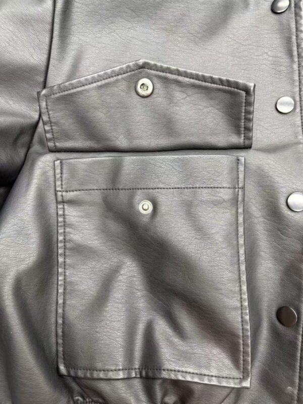 Close-up of a silver leather jacket featuring two front pockets with snap buttons, showcasing high-quality material and trendy design.