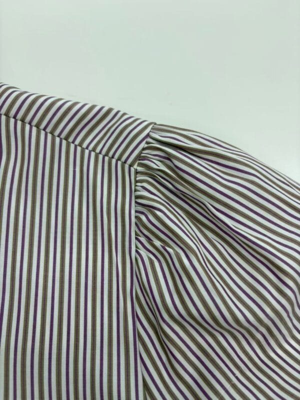 Close-up of striped fabric with purple, green, and white lines, showcasing detailed stitching and texture for fashion design.