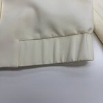 Close-up of cream-colored fabric with smooth texture and subtle sheen, showcasing fine stitching and high-quality material.