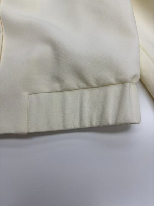 Close-up of cream-colored fabric with smooth texture and subtle sheen, showcasing fine stitching and high-quality material.