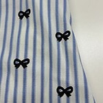 Close-up of a blue and white striped dress featuring small black bow embellishments along the fabric.