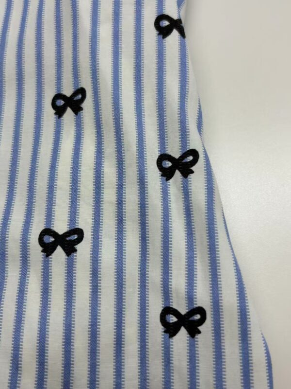 Close-up of a blue and white striped dress featuring small black bow embellishments along the fabric.
