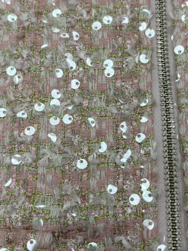 Close-up of pink fabric with intricate embroidery and shiny sequins, featuring a silver zipper on the side, suitable for fashion and couture designs.