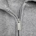 Close-up of a gray zip-up hoodie with a silver zipper and ribbed collar, made from soft cotton fabric.
