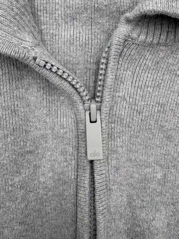 Close-up of a gray zip-up hoodie with a silver zipper and ribbed collar, made from soft cotton fabric.