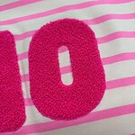Close-up of a pink, textured number zero on a white fabric with pink horizontal stripes, suitable for children's clothing or accessories.