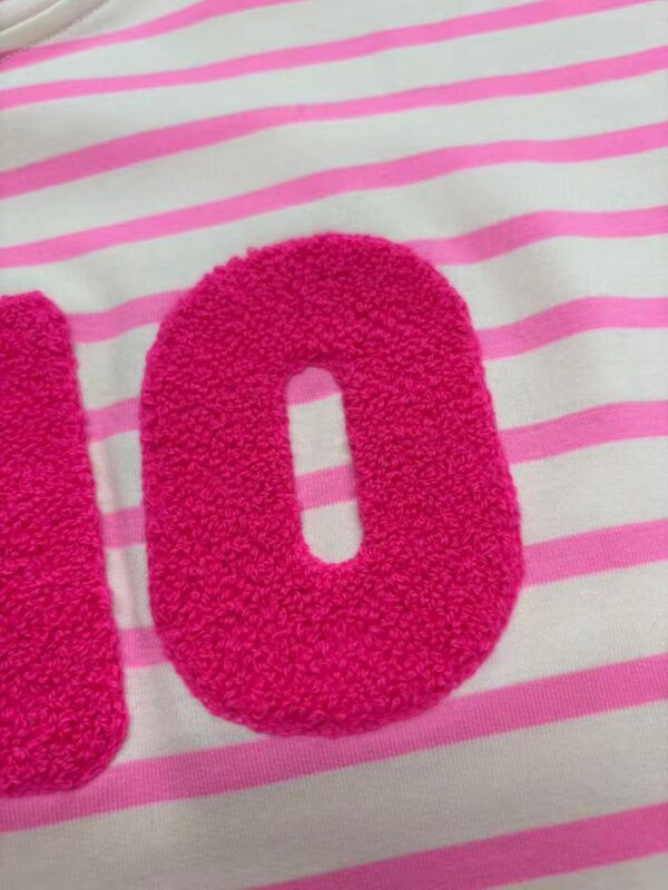 Close-up of a pink, textured number zero on a white fabric with pink horizontal stripes, suitable for children's clothing or accessories.