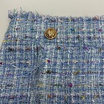 Close-up of a stylish tweed fabric with multicolored threads and a gold decorative button, perfect for high-end fashion designs.