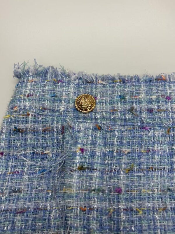 Close-up of a stylish tweed fabric with multicolored threads and a gold decorative button, perfect for high-end fashion designs.