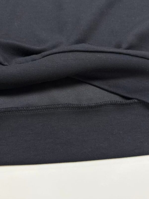 Close-up image of black fabric material showing texture and stitching details, suitable for fashion or clothing product descriptions.