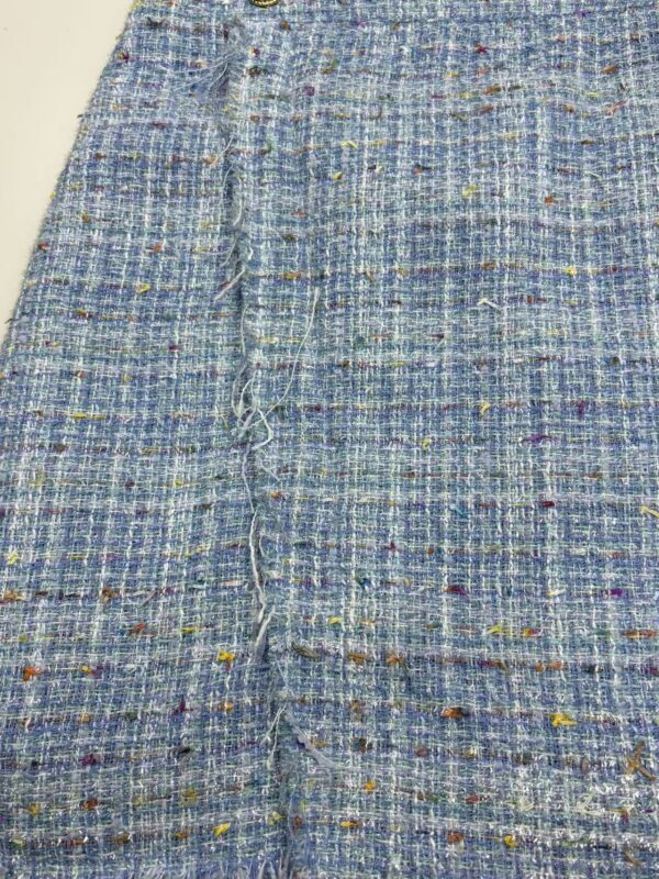 Close-up of vibrant tweed fabric with multicolored threads, showcasing texture and intricate weaving suitable for high-end fashion designs.