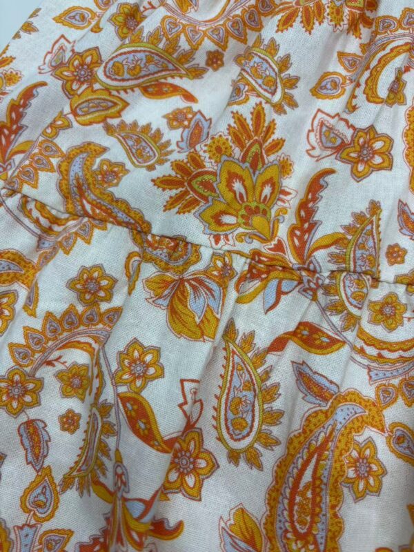 Close-up of bohemian paisley fabric with orange, yellow, and white floral patterns, showcasing detailed design and vibrant colors.