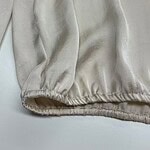 Close-up of cream satin fabric with soft sheen and gathered elastic hem, showcasing luxurious texture and high-quality material for fashion design.