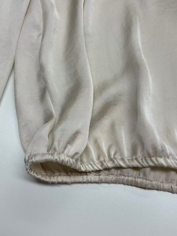 Close-up of cream satin fabric with soft sheen and gathered elastic hem, showcasing luxurious texture and high-quality material for fashion design.