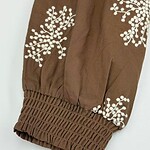 Close-up of brown fabric sleeve with white embroidered floral pattern and elasticated cuff, showcasing detailed craftsmanship.