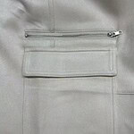 Close-up of a light grey jacket featuring a horizontal zipper pocket and a large rectangular pocket below it, made of smooth fabric.