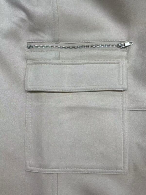 Close-up of a light grey jacket featuring a horizontal zipper pocket and a large rectangular pocket below it, made of smooth fabric.