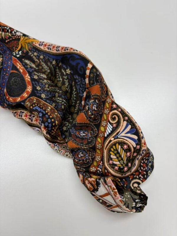 Close-up of a fabric sleeve with vibrant paisley and floral patterns in orange, blue, black, and beige, showcasing detailed textile design.