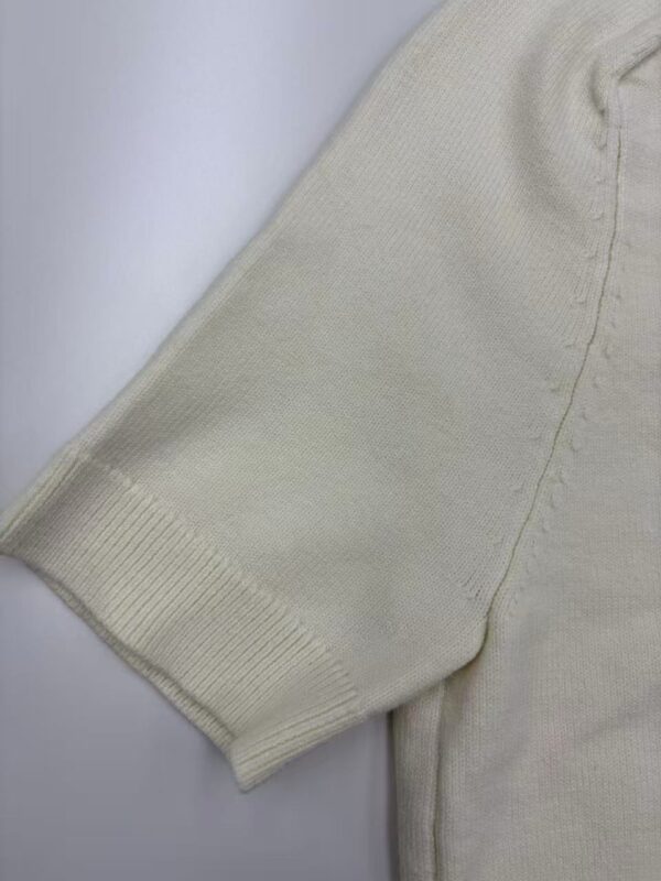 Close-up of a cream-colored sweater sleeve showing ribbed cuff and soft knit fabric, ideal for casual or stylish winter wear.
