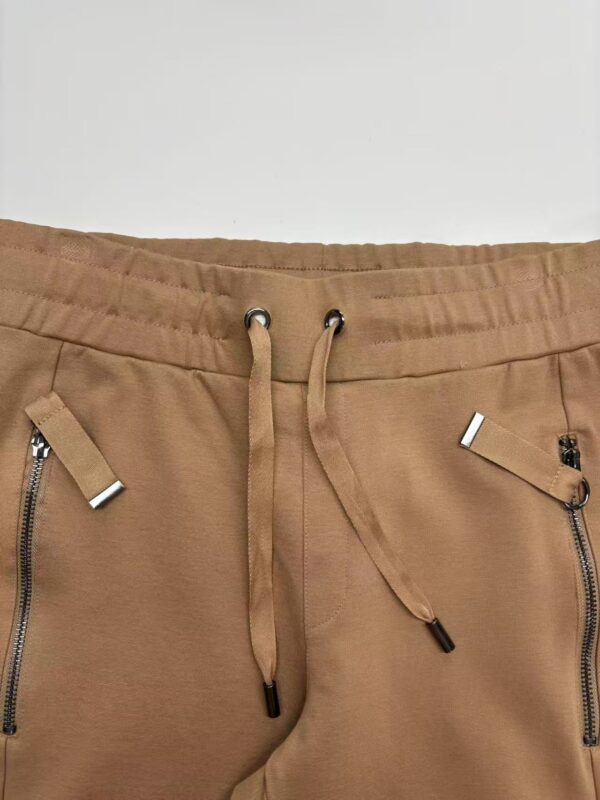 Close-up of men's beige jogger pants with zippered pockets and drawstring waistband, suitable for casual wear and athletic activities.