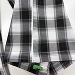 Close-up of a black, white, and gray plaid flannel shirt with a zipper and green toggle at the bottom hem, suitable for casual fashion.