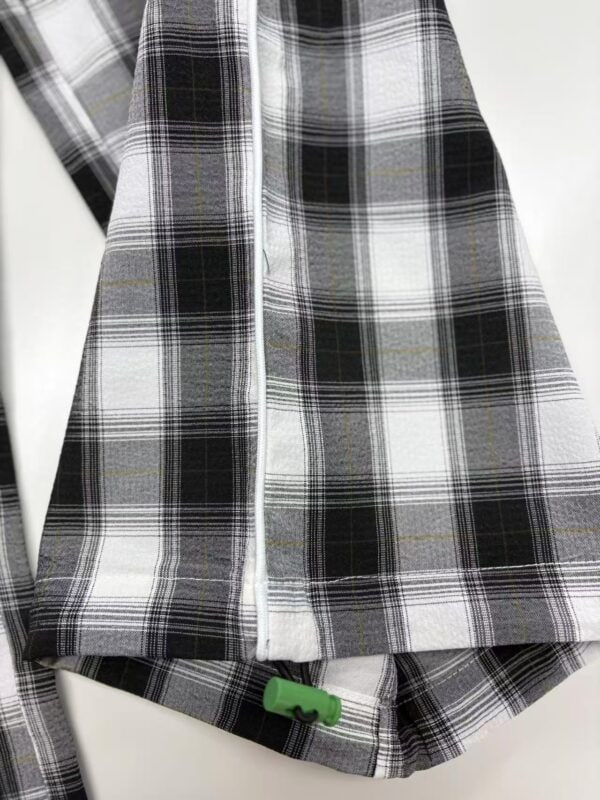 Close-up of a black, white, and gray plaid flannel shirt with a zipper and green toggle at the bottom hem, suitable for casual fashion.