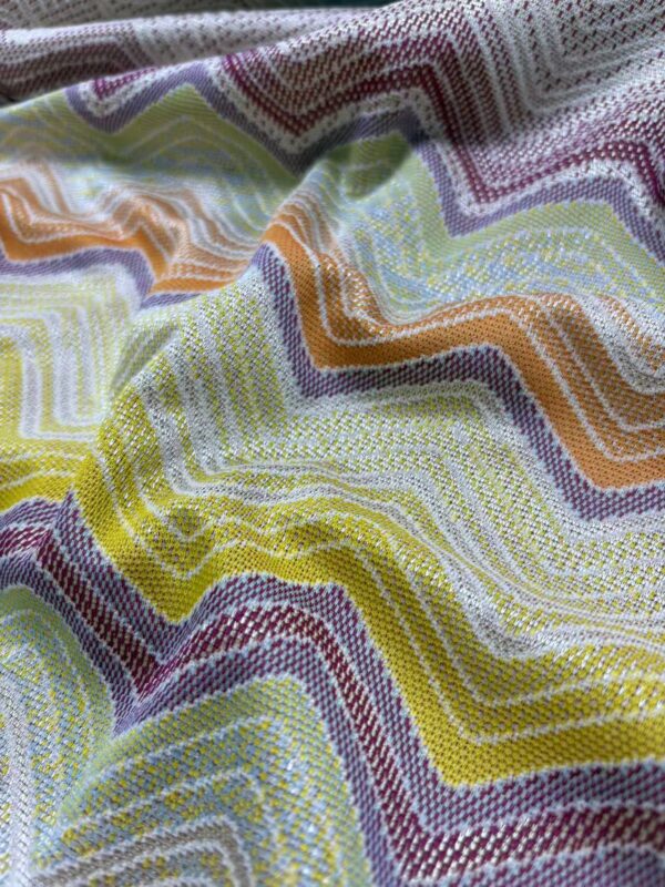 Close-up of vibrant, multicolored fabric with wavy, zigzag pattern, showcasing detailed stitching and texture, ideal for fashion and textile design.