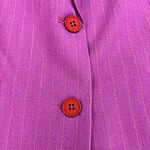 Close-up of a pink pinstripe suit with red buttons, showcasing fine fabric texture and tailored stitching for a stylish professional look.