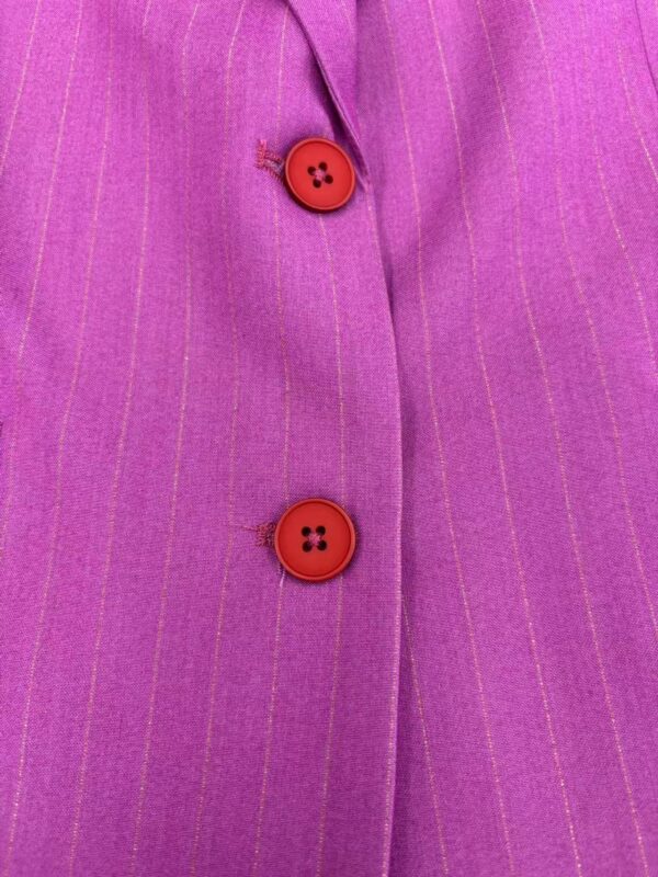 Close-up of a pink pinstripe suit with red buttons, showcasing fine fabric texture and tailored stitching for a stylish professional look.