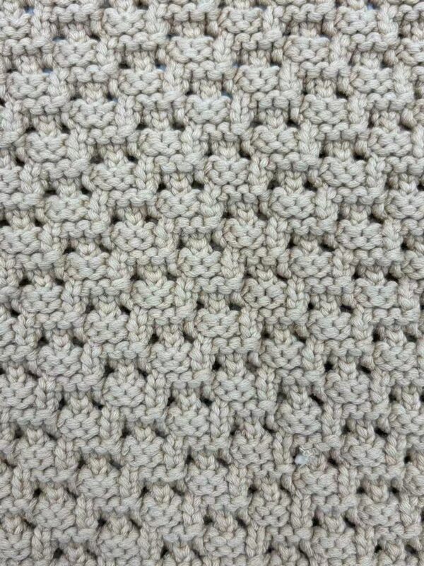 Close-up of a beige, textured knitted fabric with a detailed pattern, ideal for fashion and apparel design.