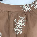 Close-up of a brown skirt featuring intricate white embroidery floral patterns at the waist and hem, showcasing stylish and detailed design.